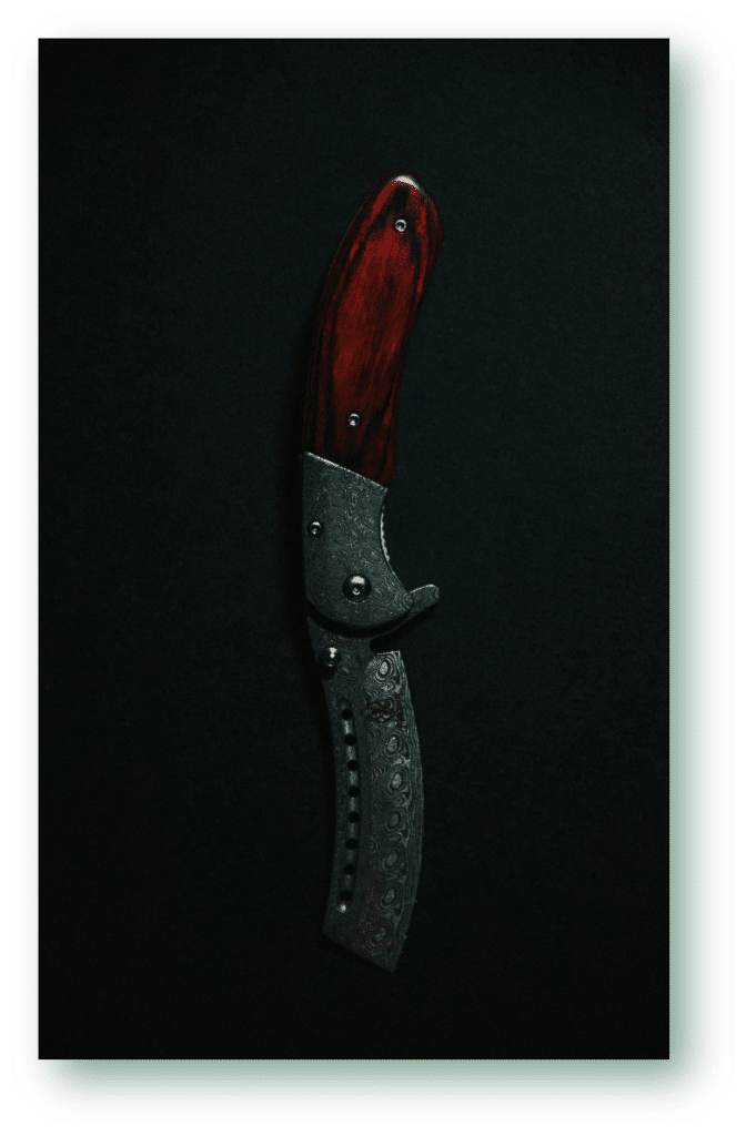 Damascus folding knife with a red wood handle on a dark background