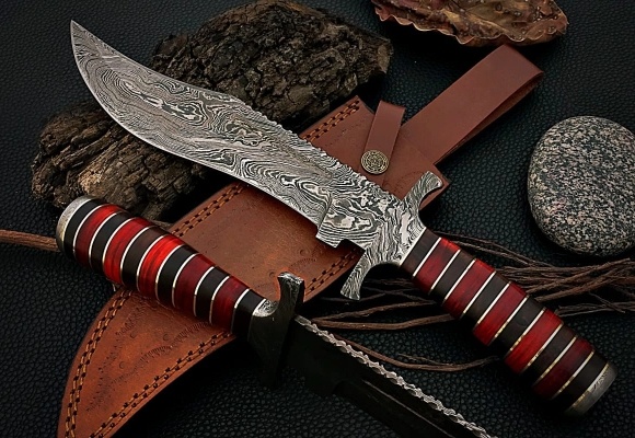 Damascus hunting knife with a red handle and leather sheath on a dark background